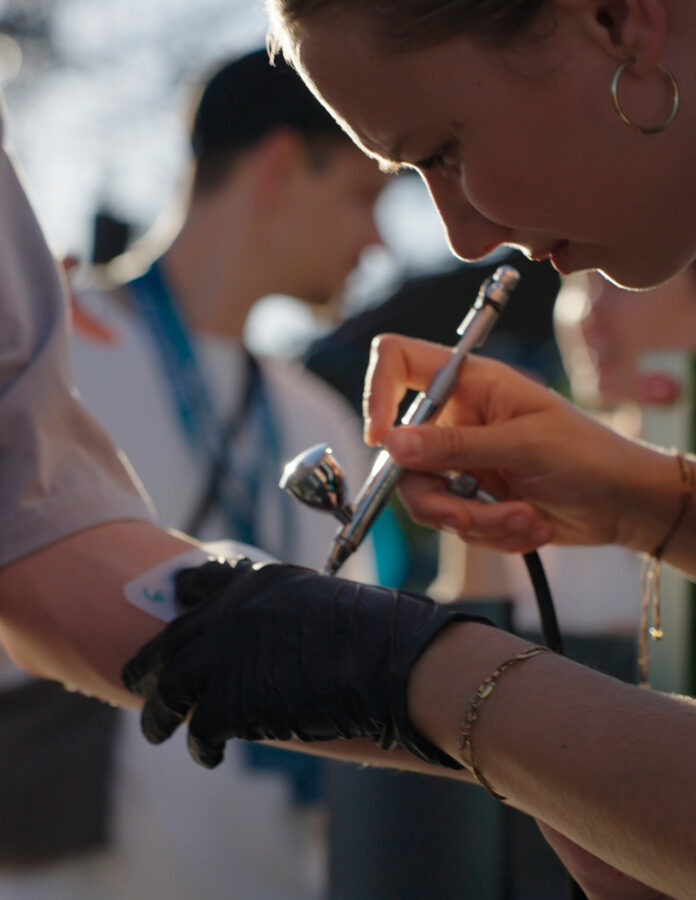 Artista aplicando un tatuaje temporal con aerógrafo en el brazo de un asistente en la House of IQOS de Zamna Madrid