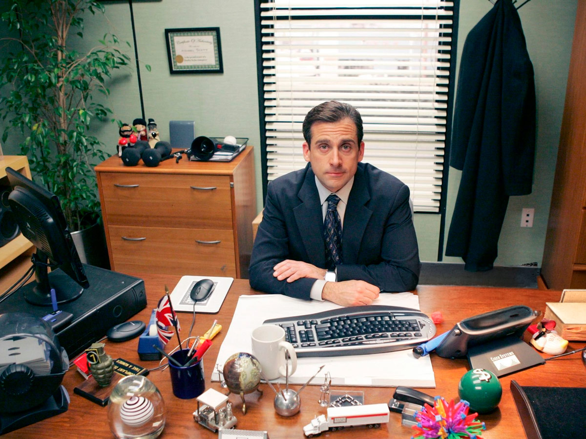 Steve Carell como Michael Scott en su mesa de trabajo