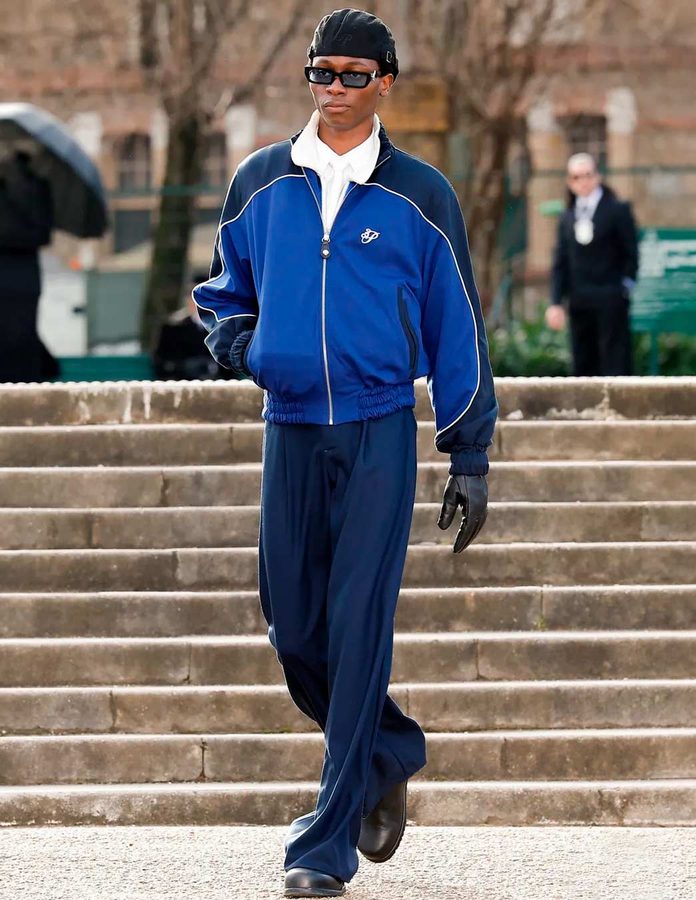 Modelo de 3.Paradis con chaqueta deportiva azul, pantalón marino amplio, camisa blanca, botas negras, guantes de cuero y boina.