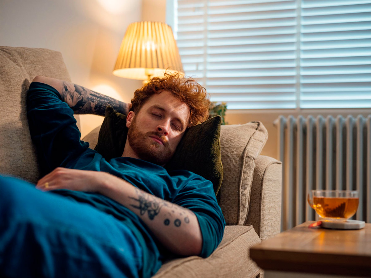 hombre dormido en sofá con bebida caliente encima de la mesa
