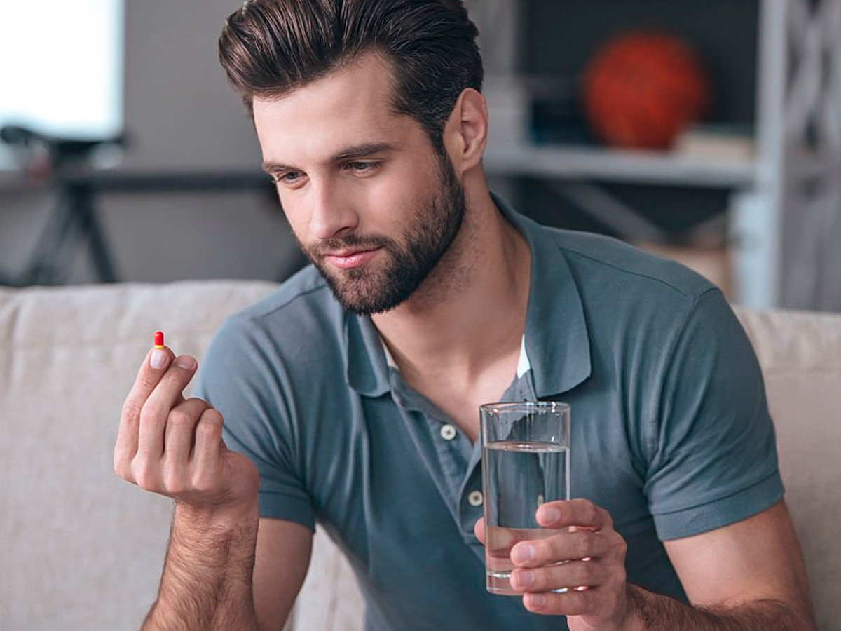 hombre joven con cápsula y vaso de agua en la mano