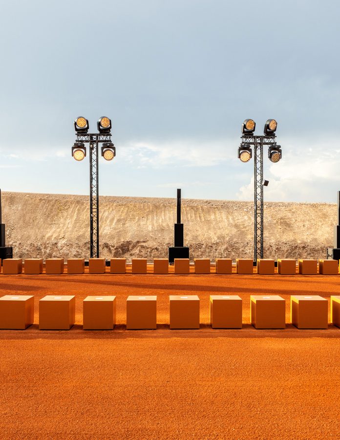 Escenario del desfile de Giorgio Armani & Kith en el desierto de Agafay con asientos naranjas y torres de luz