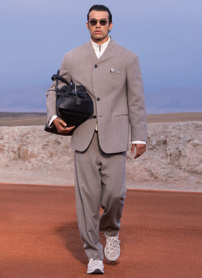 Modelo con traje de lana de espiga gris claro, bolso de piel negro y zapatillas ASICS de Giorgio Armani & Kith