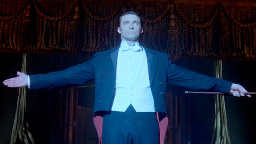 Hugh Jackman como el mago Robert Angier con los brazos abiertos sobre el escenario en The Prestige, imagen del teaser del reestreno de 2027