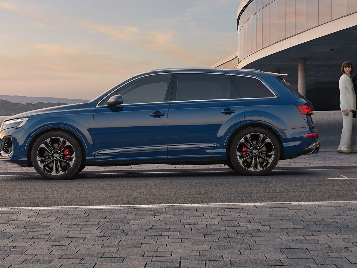 Audi Q7 renovado azul de perfil frente a un edificio con dos personas
