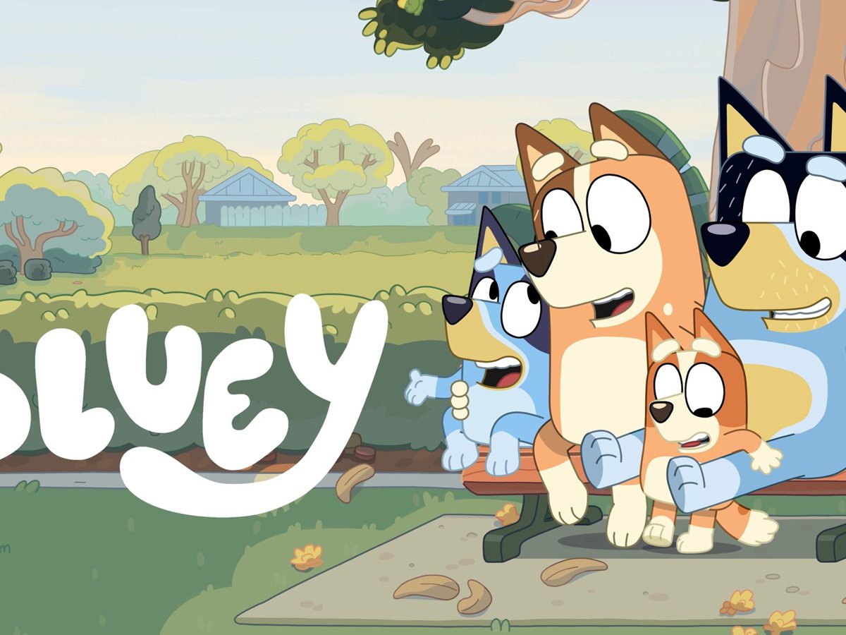 Bluey, Bingo, Chilli y Bandit, la familia Heeler de la serie Bluey, sentados en un banco de parque junto al logotipo de la serie