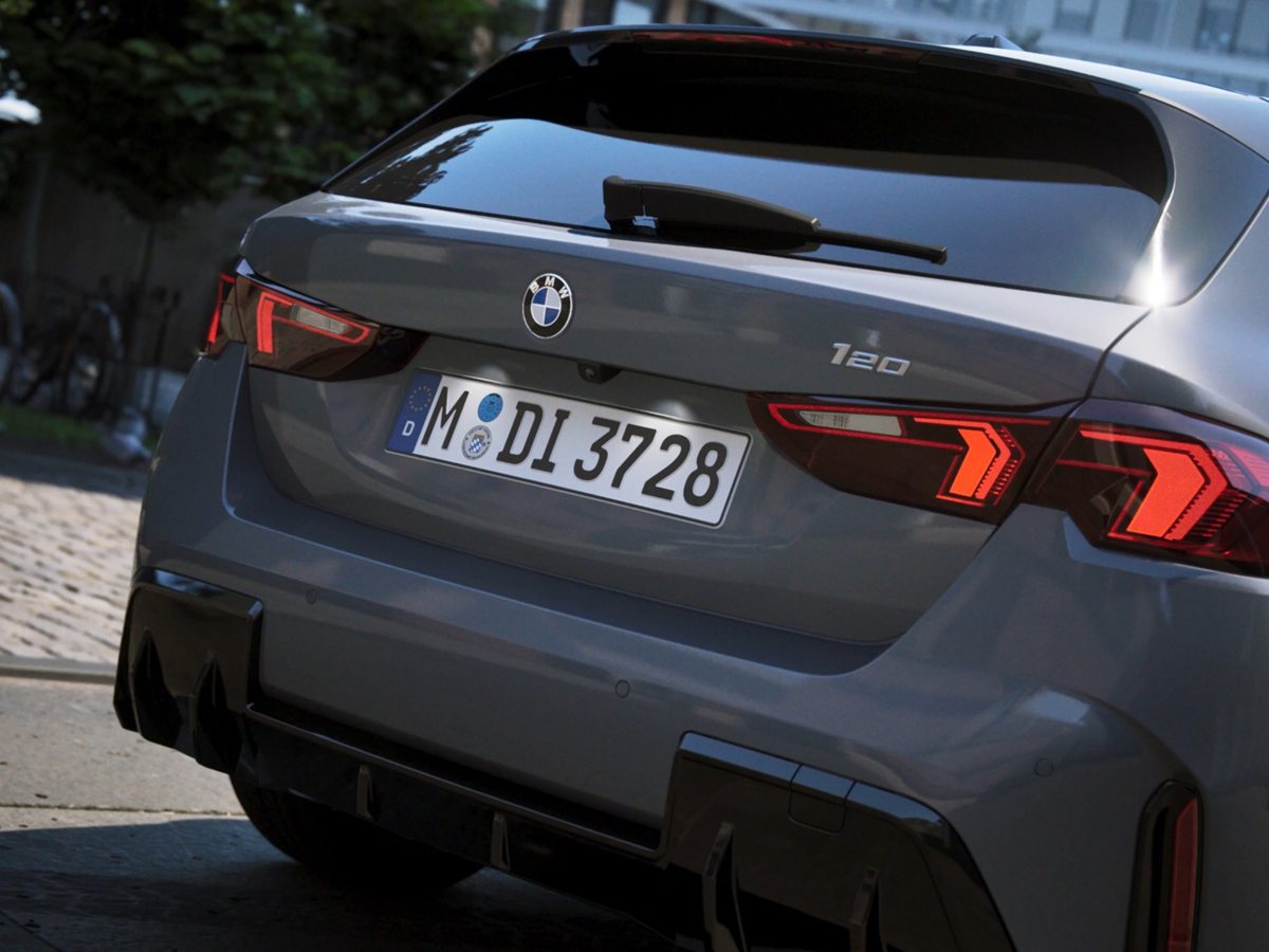 BMW 120 gris visto desde atrás en una calle adoquinada con los pilotos encendidos