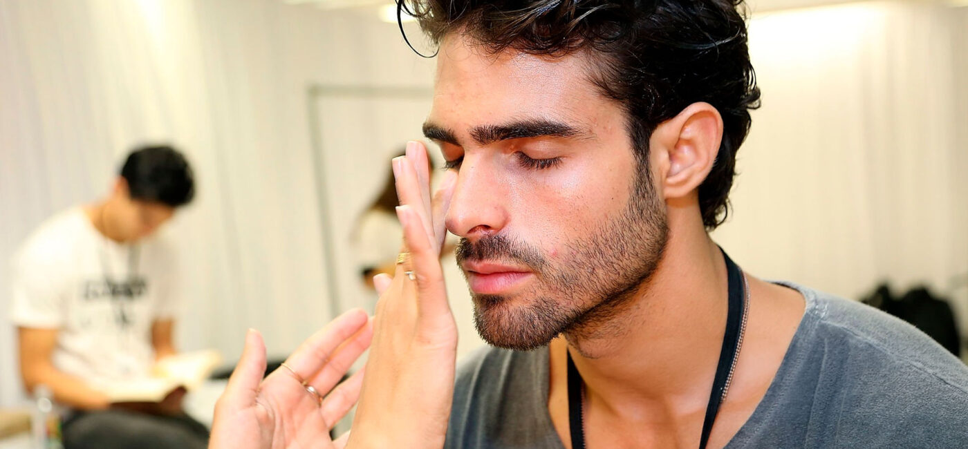 Modelo Juan Bettancourt poniéndose crema en la cara en backstage desfile