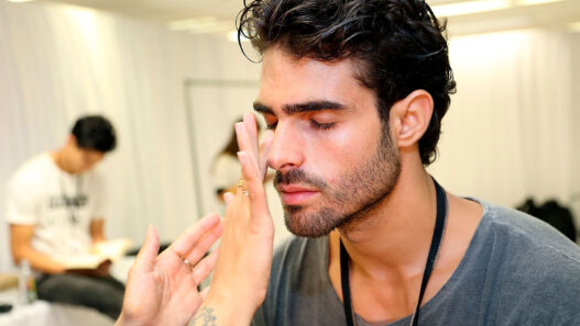 Modelo Juan Bettancourt poniéndose crema en la cara en backstage desfile