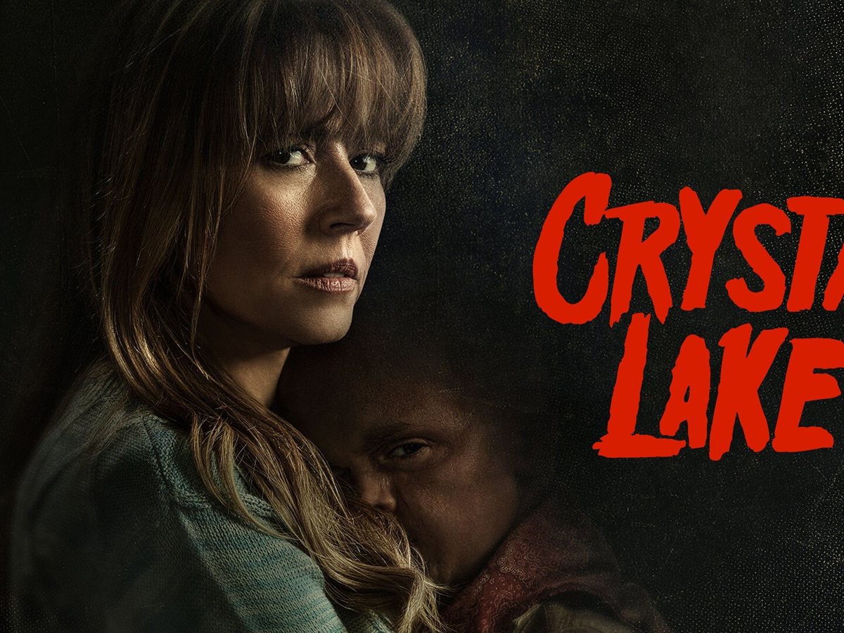 Linda Cardellini, como Pamela Voorhees, sostiene a un niño contra el pecho junto al logotipo rojo de Crystal Lake