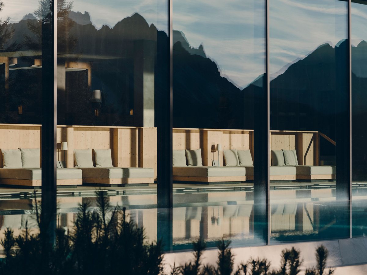 Piscina del spa de FORESTIS con camas balinesas de madera y los Dolomitas reflejados en la cristalera