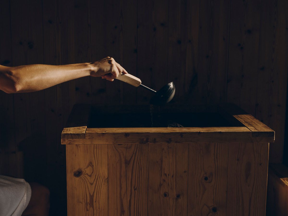 Brazo vertiendo agua con un cazo sobre la estufa de madera de una sauna de FORESTIS