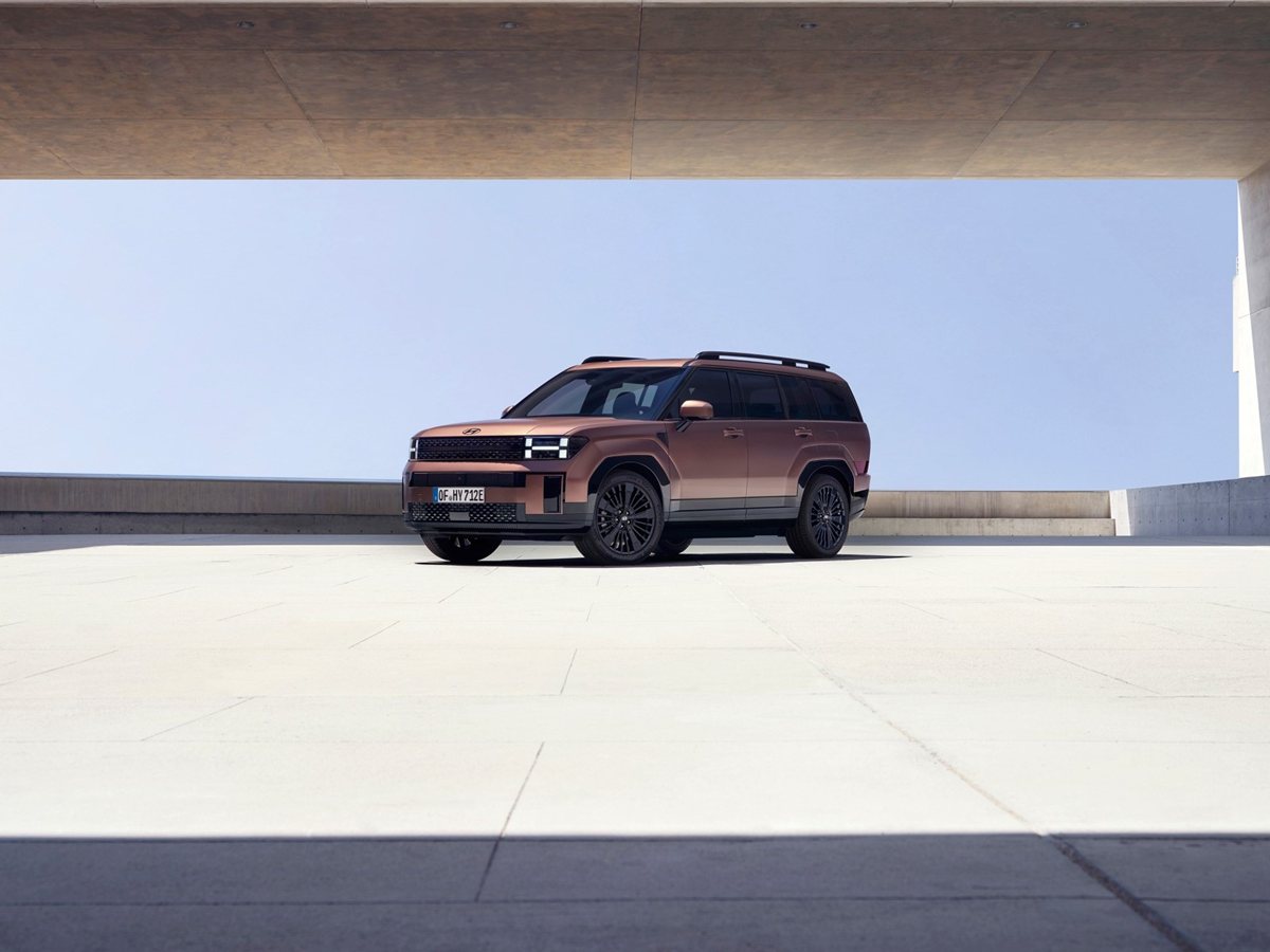 Hyundai Santa Fe híbrido enchufable de color cobre de tres cuartos delantero bajo un edificio de hormigón