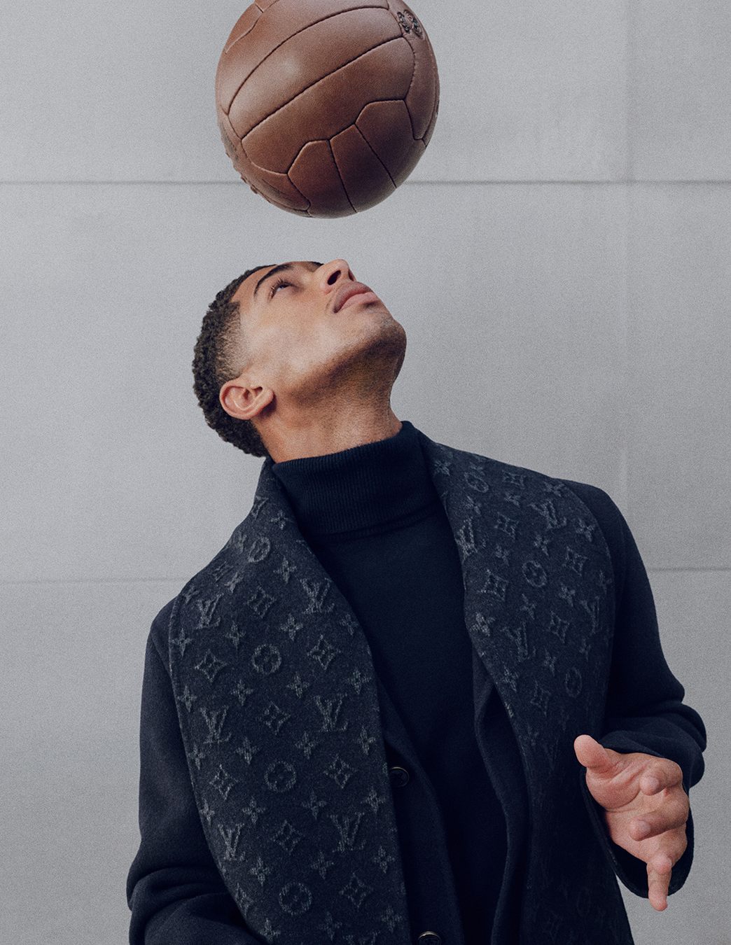 Jude Bellingham con el abrigo de cachemira y la bufanda Monogram de Louis Vuitton, cabeceando un balón de cuero