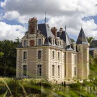 Château du Breuil de Les Sources de Cheverny, castillo de piedra clara con tejado de pizarra y torreón entre árboles del valle del Loira