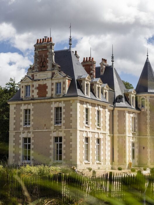 Château du Breuil de Les Sources de Cheverny, castillo de piedra clara con tejado de pizarra y torreón entre árboles del valle del Loira