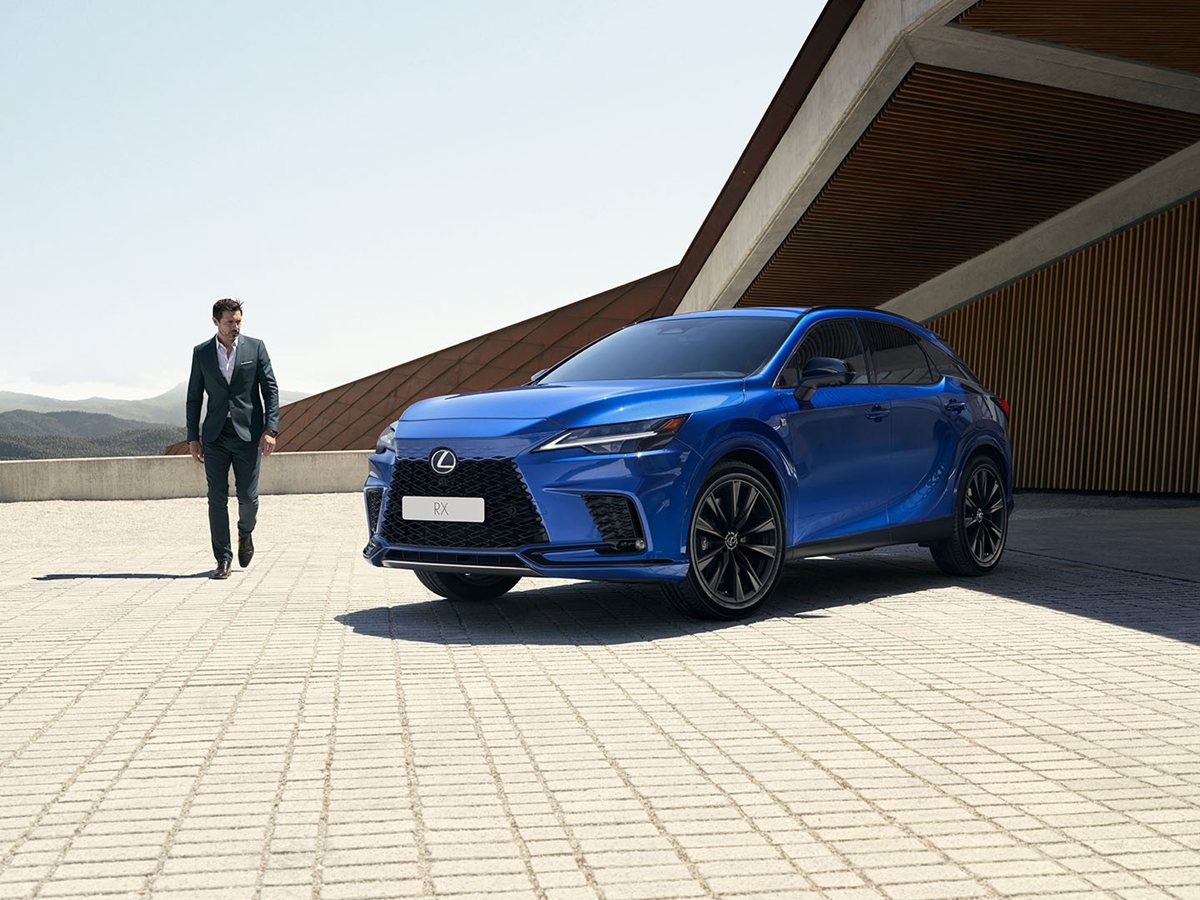 Lexus RX 450h+ azul de tres cuartos delantero en una plaza con un hombre caminando