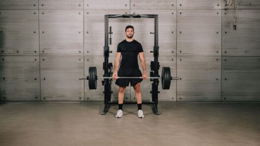 Hombre de pie con la espalda recta sujetando una barra cargada delante de un rack Technogym