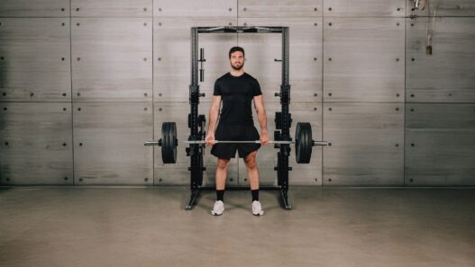 Hombre de pie con la espalda recta sujetando una barra cargada delante de un rack Technogym