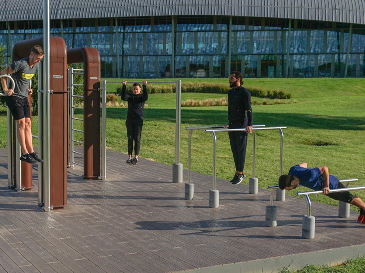 Cuatro hombres entrenando en una estación de calistenia al aire libre con anillas, barra de dominadas y paralelas