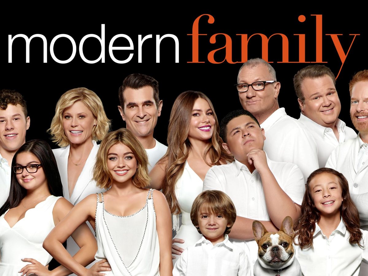 El reparto de Modern Family vestido de blanco sobre fondo negro, con Ed O'Neill, Ty Burrell, Sofía Vergara y el bulldog francés Stella