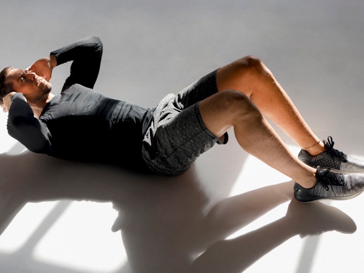 Hombre con camiseta negra haciendo abdominales en el suelo de un estudio iluminado por el sol