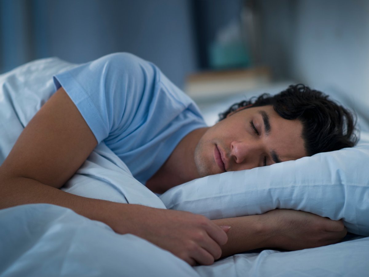 Hombre joven durmiendo de lado en una cama con sábanas azules