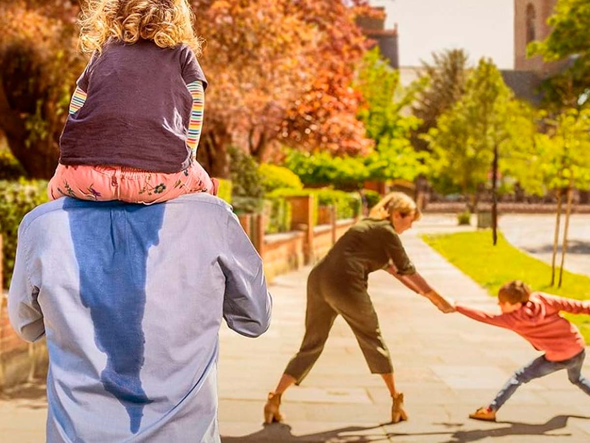 Cartel de Bendita paciencia (Breeders): Ally, interpretada por Daisy Haggard, tira del brazo de su hijo en una acera mientras Paul lleva a la niña a hombros