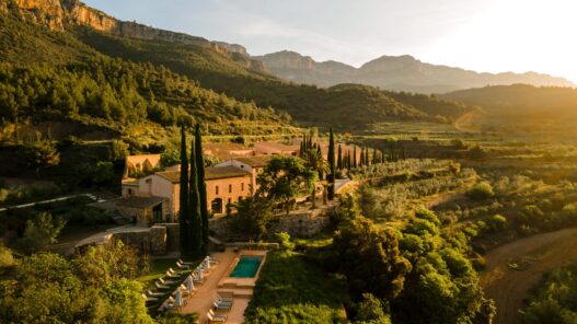 Terra Dominicata, hotel y bodega del Priorat visto desde el aire al atardecer con la sierra del Montsant al fondo y la piscina entre cipreses