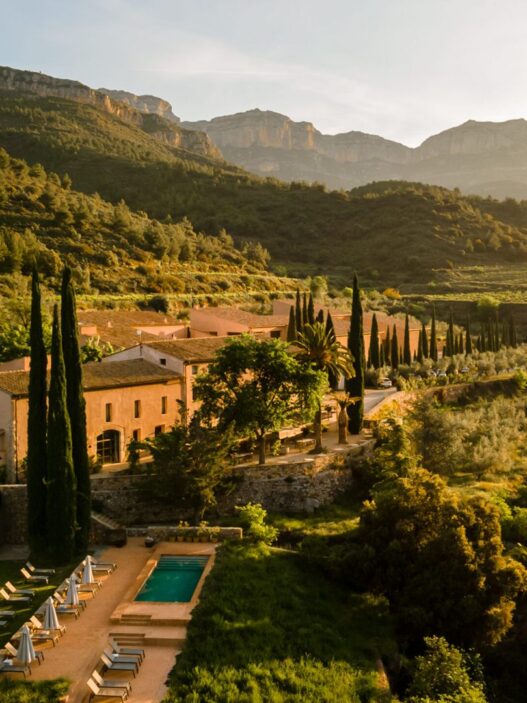 Terra Dominicata, hotel y bodega del Priorat visto desde el aire al atardecer con la sierra del Montsant al fondo y la piscina entre cipreses