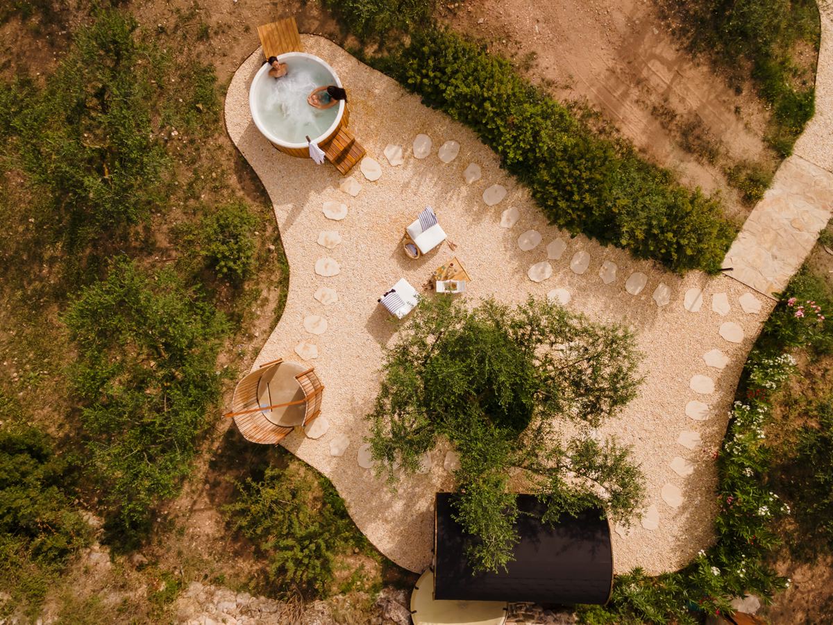 Vista aérea del spa exterior Les Oliveres de Terra Dominicata con la bañera nórdica, la sauna de barril y la zona de relax entre olivos