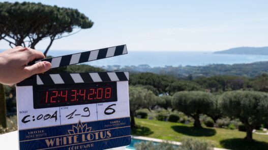 Claqueta del rodaje de The White Lotus temporada 4 con el logotipo White Lotus Côte d'Azur, con los pinos y el mar de la Riviera francesa al fondo