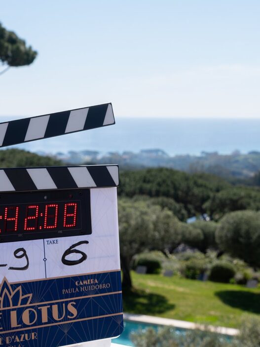 Claqueta del rodaje de The White Lotus temporada 4 con el logotipo White Lotus Côte d'Azur, con los pinos y el mar de la Riviera francesa al fondo