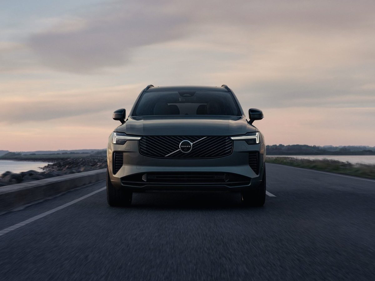 Volvo XC90 híbrido enchufable gris de frente circulando por una carretera junto al mar al atardecer